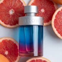 Vibrant gradient perfume bottle surrounded by fresh grapefruits, colorful and eye-catching.
