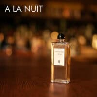a 50ml bottle of Serge Lutens A La Nuit Eau de Parfum with a tall, rectangular black glass design and a gold cap on a brown table.