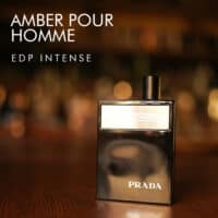 A 100ml bottle of Prada Amber Pour Homme Intense Eau de Parfum (Discontinued - Batch 2019) with a dark amber-colored glass design and a black cap, placed on a brown table.
