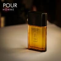 A 100ml bottle of Azzaro Pour Homme Eau de Toilette with a square glass bottle, gold tinted lass and black cap on a brown table.
