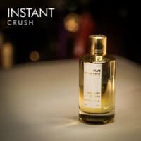 A 120ml bottle of Mancera Instant Crush Eau de Parfum with a gradient gold and clear glass design and a gold cap on a brown table.