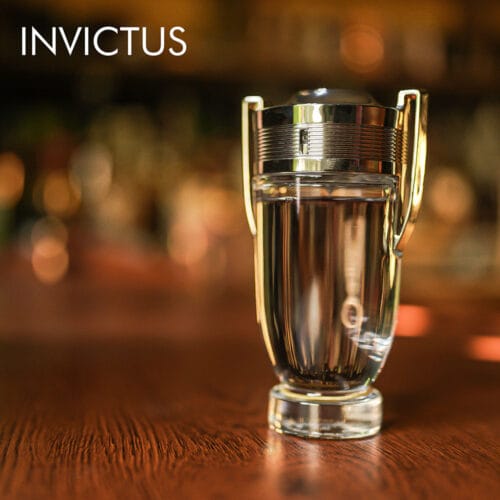 A 100ml bottle of Paco Rabanne Invictus Eau de Toilette with a silver trophy-shaped design in silver and clear glass, placed on a brown table.