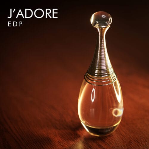 A 100ml bottle of Dior J’adore Eau de Parfum with a tall, golden collar, a rounded glass bottle, and a transparent base on a brown table.