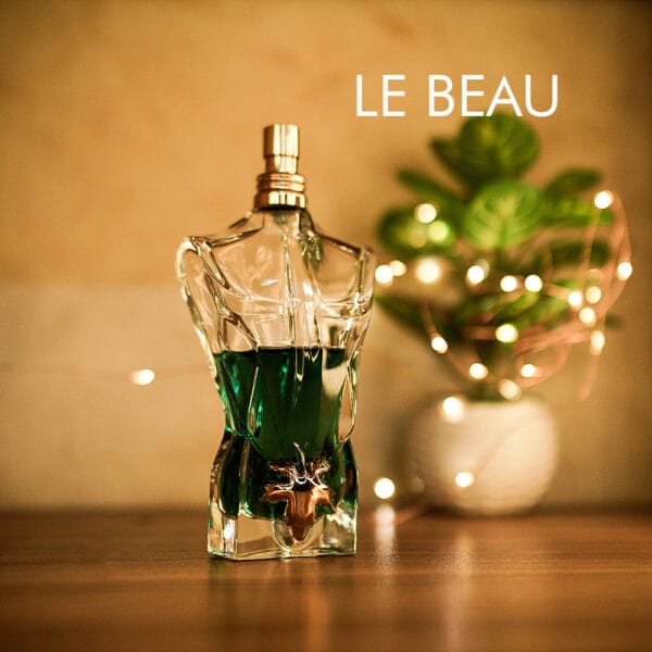 A 75ml bottle of Jean Paul Gaultier Le Beau Eau de Toilette, shaped like a male torso with a gold-tone collar, green liquid, placed on a brown table.