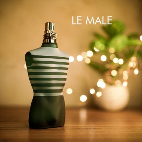 A 125ml bottle of Jean Paul Gaultier Le Male Eau de Toilette, shaped like a male torso in blue with white stripes, placed on a brown table.