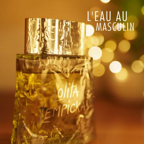 A 100ml bottle of Lolita Lempicka L’Eau Au Masculin (Vintage) Eau de Toilette, shaped like a frosted glass cylinder with leaf engravings and a silver-toned cap, placed on a brown table.