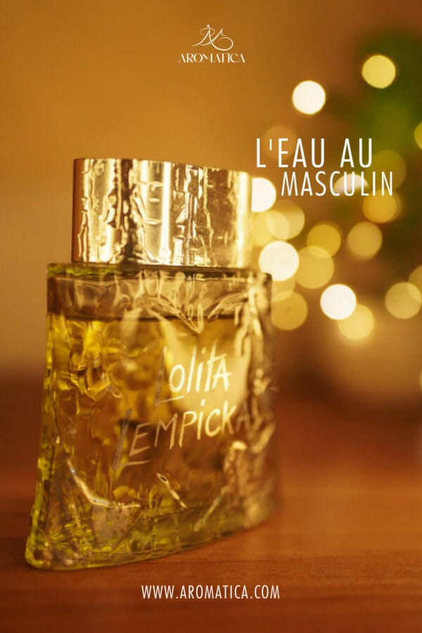 A 100ml bottle of Lolita Lempicka L’Eau Au Masculin (Vintage) Eau de Toilette, shaped like a frosted glass cylinder with leaf engravings and a silver-toned cap, placed on a brown table.