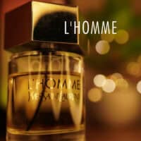 A 100ml bottle of Yves Saint Laurent L’Homme Eau de Toilette - Batch 2015 with a silver cap and clear glass bottle on a brown table.