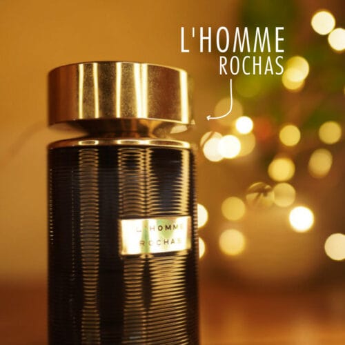 A 100ml bottle of Rochas L’Homme Eau de Toilette with a cylindrical blue glass design and silver cap, placed on a brown table.