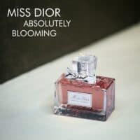 A clear bottle with light red liquid and a silver ribbon of Miss Dior Absolutely Blooming Eau De Parfum with silver font labels.