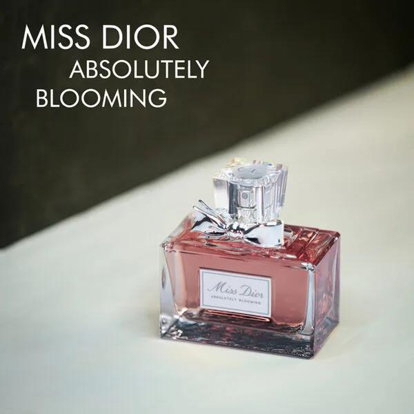 A clear bottle with light red liquid and a silver ribbon of Miss Dior Absolutely Blooming Eau De Parfum with silver font labels.