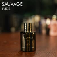 A 60ml bottle of Dior Sauvage Elixir with a dark blue glass bottle, dark-colored cap, on a brown table.
