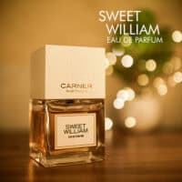 A 100ml bottle of Carnar Barcelona Sweet William Eau de Parfum with a square glass design and white cap on a brown table.