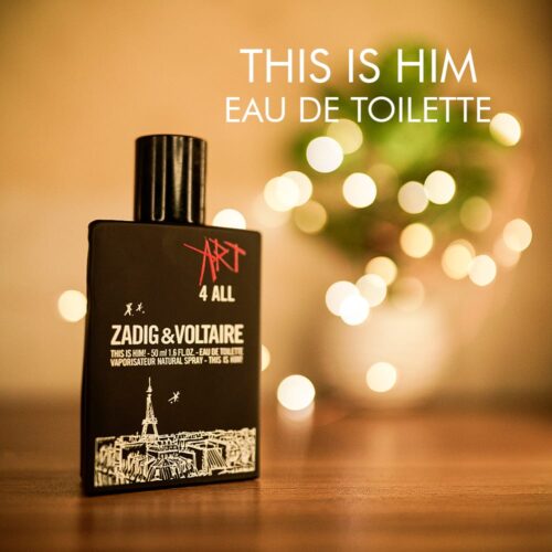 A 100ml bottle of Zadig & Voltaire This Is Him Eau de Toilette with a square dark glass body, white label, and black cap on a brown table.