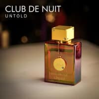 A 105ml bottle of Armaf Club de Nuit Untold Eau de Parfum with a transparent semi gold glass bottle and gold cap on a brown table.