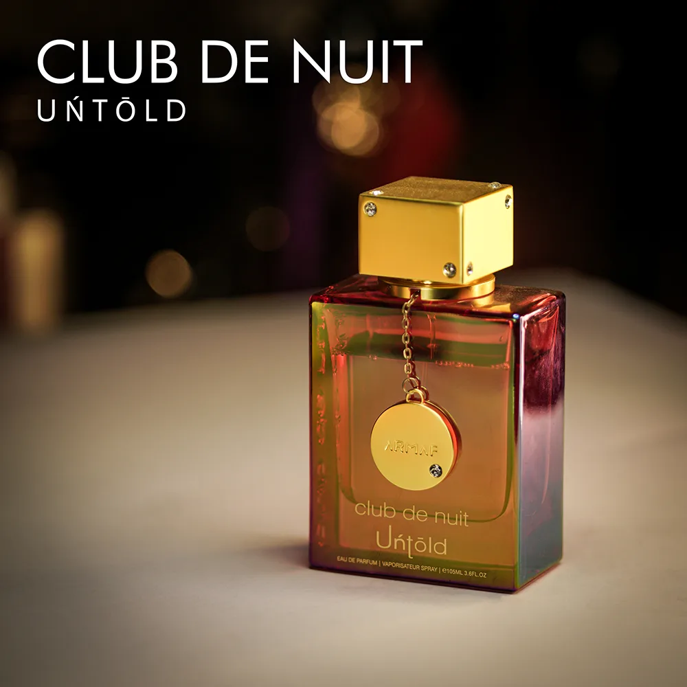 A 105ml bottle of Armaf Club de Nuit Untold Eau de Parfum with a transparent semi gold glass bottle and gold cap on a brown table.