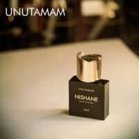 A 50ml bottle of Nishane Unutamam (Batch 2020) Extrait de Parfum with a sleek, dark bottle featuring gold detailing, placed on a white table.