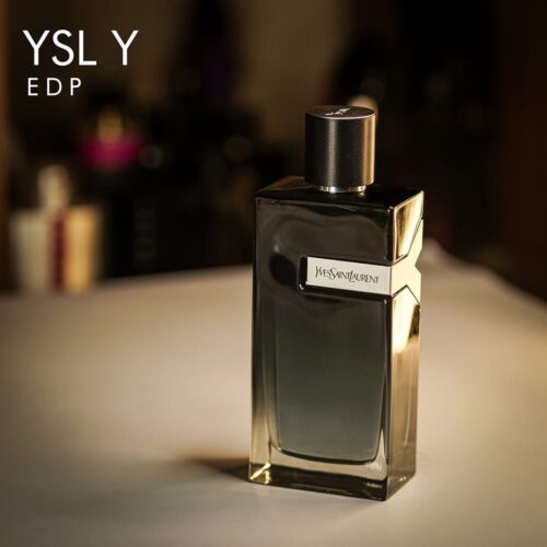 a 100ml bottle of Yves Saint Laurent Y Eau de Parfum with a sleek rectangular blue glass design, a silver "Y" logo on the side, and a black cap on a brown table.