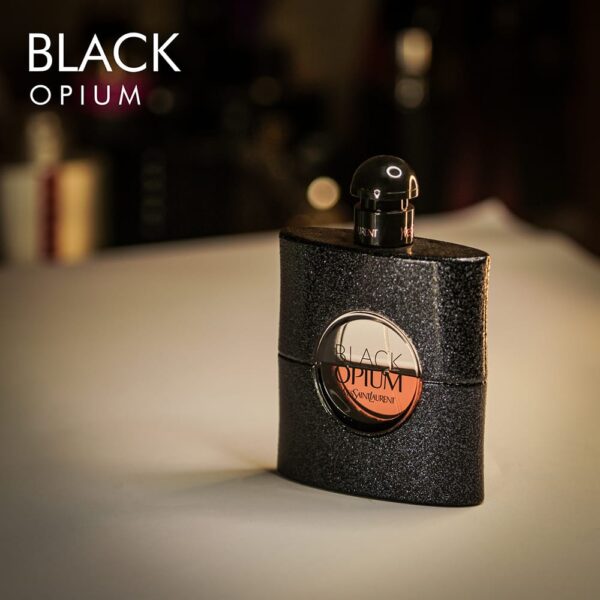 a 90ml bottle of Yves Saint Laurent Black Opium Eau de Parfum with a round black glass design featuring a glittery black circle in the center and a black cap on a brown table.