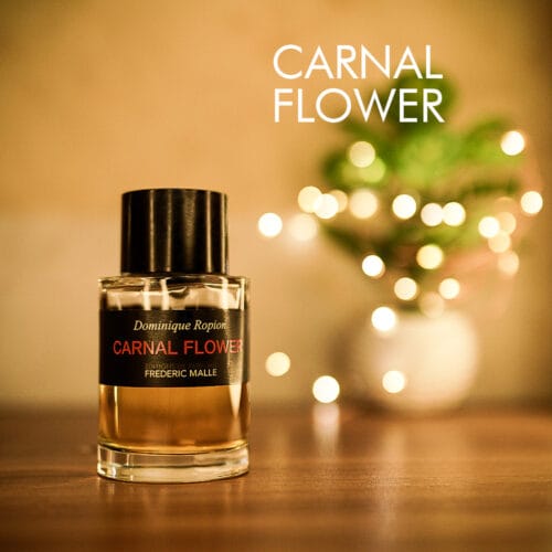 a 100ml bottle of Frédéric Malle Carnal Flower Eau de Parfum with a cylindrical clear glass design, and a black cap on a brown table.