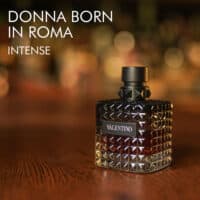 a 100ml bottle of Valentino Donna Born In Roma Intense Eau de Parfum with a black studded glass design and black cap on a brown table