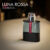 a 100ml bottle of Prada Luna Rossa Carbon Eau de Toilette with a sleek gray glass design, red branding, and a clear cap on a brown table.