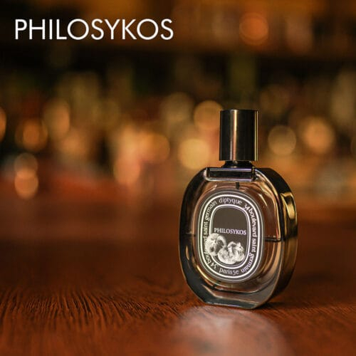 a 100ml bottle of Diptyque Philosykos Eau de Parfum with a clear glass design and black cap on a brown table.