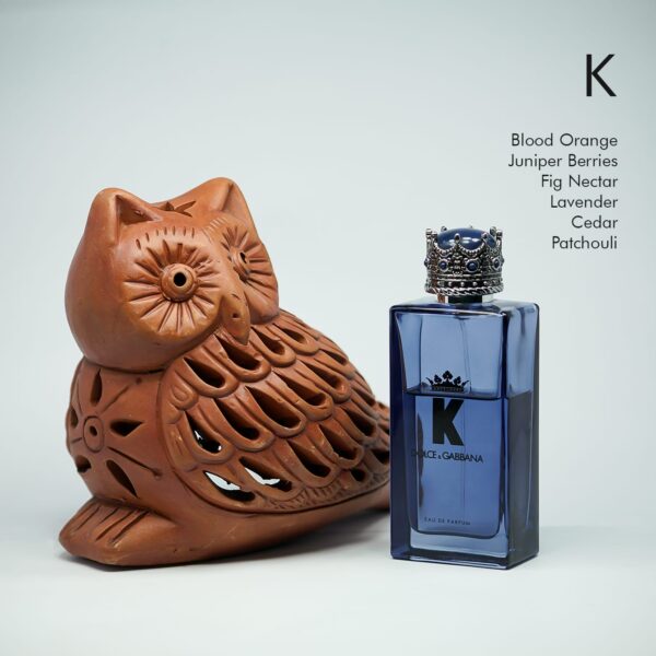 A 100ml bottle of Dolce & Gabbana K Eau de Parfum with a clear tinted glass bottle, ornate cap, on a white table.