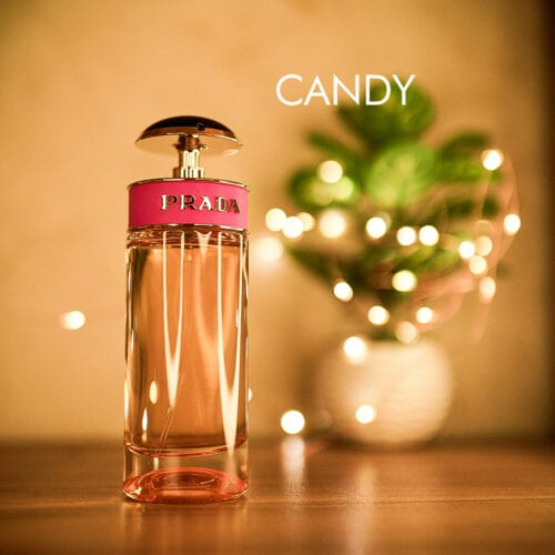 a 80ml bottle of Prada Candy Eau de Parfum with a pink glass design, gold accents, and a gold cap on a brown table