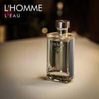 a 100ml bottle of Prada L’Homme L’Eau Eau de Toilette with a light blue glass design and silver cap on a brown table