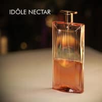 a 100ml bottle of Lancome Idole Nectar Eau de Parfum with a slim, gold-tinted glass design and gold cap on a white table
