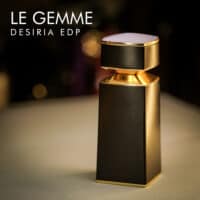 a 100ml bottle of Bvlgari Le Gemme Desiria Eau de Parfum with a purple gemstone-inspired glass design and gold cap on a white table