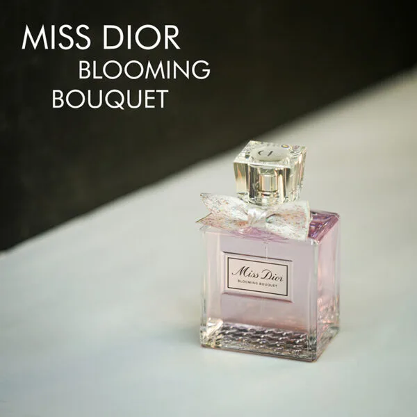 A clear bottle with light pink liquid and a cream ribbon of Miss Dior Blooming Bouquet Eau De Parfum with black font labels.