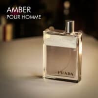 A 100ml bottle of Prada Amber Pour Homme Eau de Toilette with a clear design and a black cap on a white table