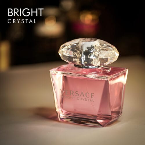 A 100ml bottle of Versace Bright Crystal Eau de Toilette with a pink design and a clear cap on a white table