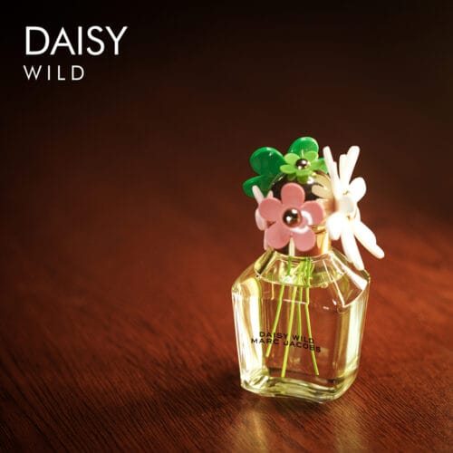 A 100ml bottle of Marc Jacobs Daisy Wild Eau de Parfum with a floral cap design and clear liquid on a brown table