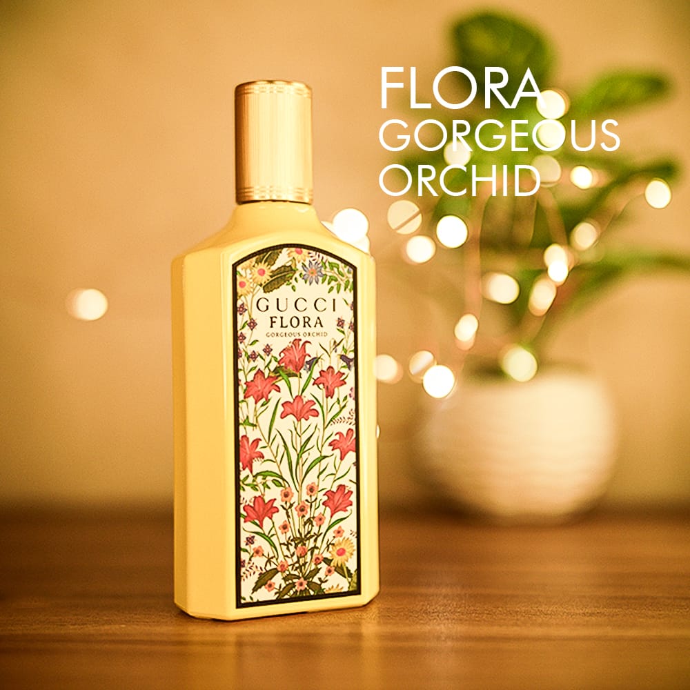 A 100ml bottle of Gucci Flora Gorgeous Orchid Eau de Parfum with a gold cap and floral design on a brown table.