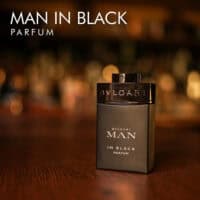 A 100ml bottle of Bvlgari Man In Black Parfum with a black and gold design on a brown table