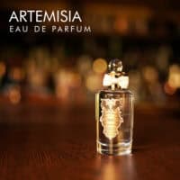 A 100ml bottle of Penhaligon's Artemisia Eau de Parfum with a gold cap and clear liquid with a white label on a brown table