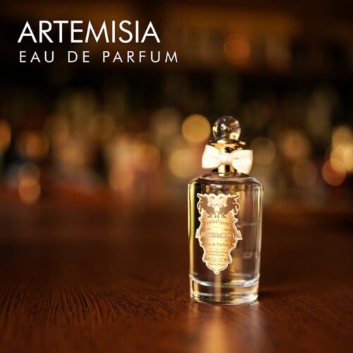 A 100ml bottle of Penhaligon's Artemisia Eau de Parfum with a gold cap and clear liquid with a white label on a brown table
