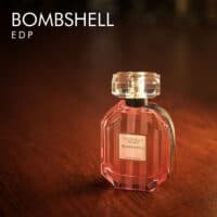 A 100ml bottle of Victoria's Secret Bombshell Eau de Parfum with a pink design and clear liquid with a white label on a brown table