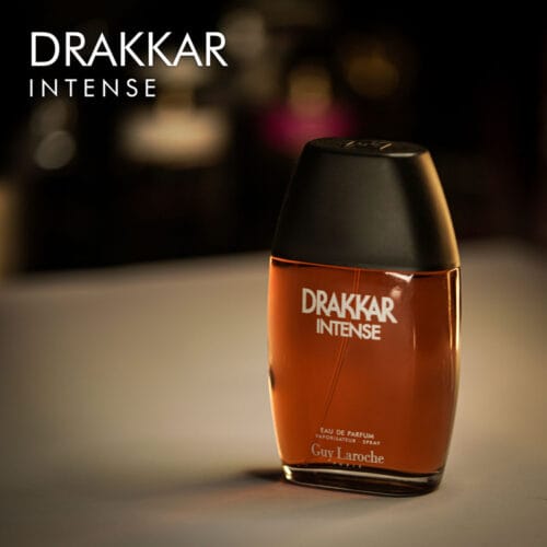 A 100ml bottle of Guy Laroche Drakkar Intense Eau de Parfum with a black cap and rusty colord liquid with white label on a brown table