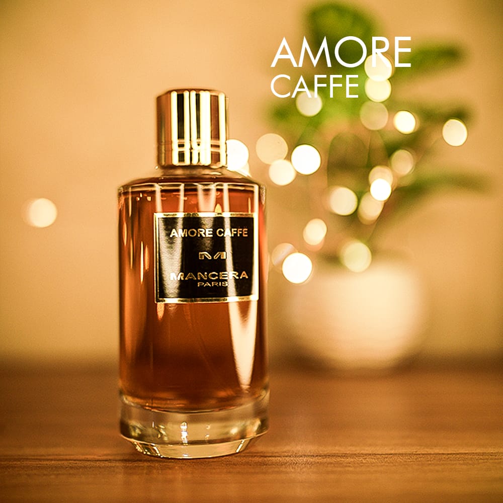 A 120ml bottle of Mancera Amore Caffè Eau de Parfum with a brown tinted glass body, a gold cap, a black label on a brown table.