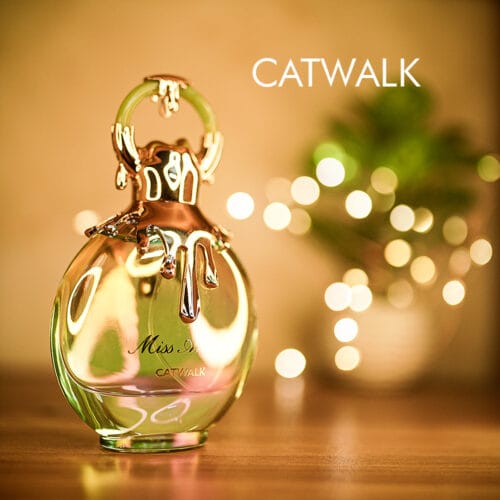 A 100ml bottle of Miss Armaf Catwalk Eau de Parfum with a gold cap and greenish design on a brown table.