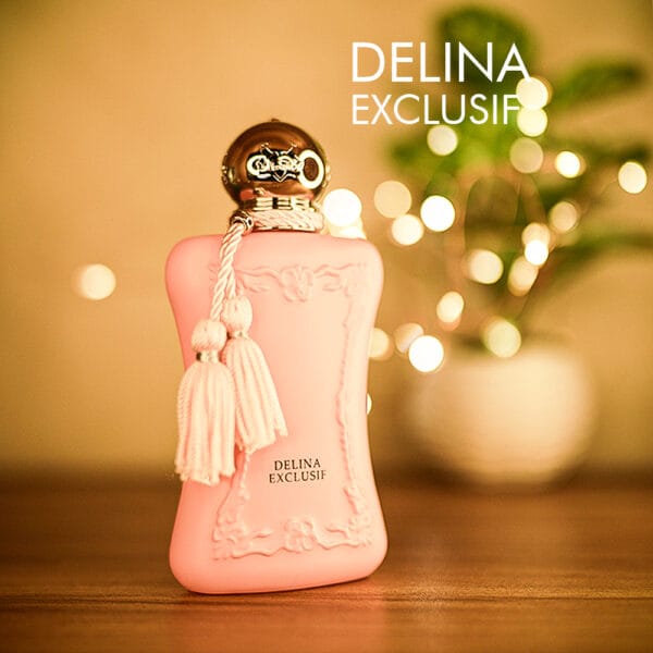 A 75ml bottle of Parfums de Marly Delina Exclusif Eau de Parfum with a pink glass body, gold detailing, and a chrome cap on a brown table.