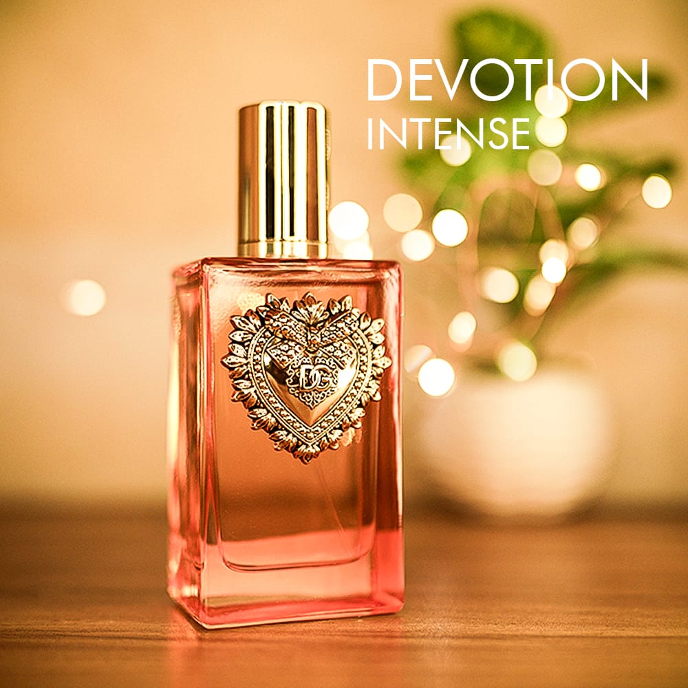 A 100ml bottle of Dolce & Gabbana Devotion Intense Eau de Parfum with a gold cap and pink bottle on a brown table.