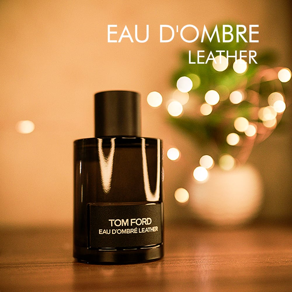 A 100ml bottle of Tom Ford Eau D'Ombre Leather Eau de Toilette with a dark amber glass body, gold label, and a black cap on a brown table.