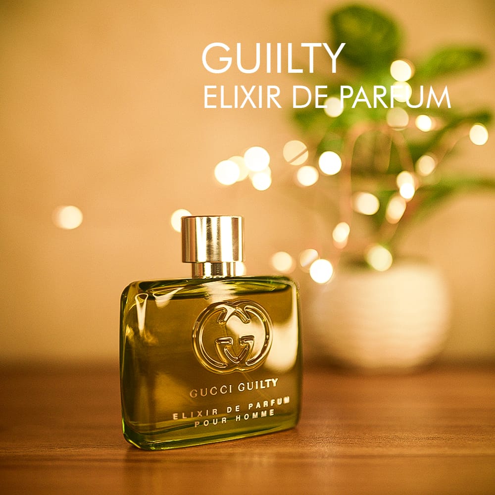 A 100ml bottle of Gucci Guilty Elixir de Parfum with a greenish glass design, a silver cap on a brown table.