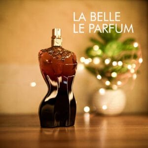 A 125mlbottle of Jean Paul Gaultier La Belle Le Parfum with a women torso shape black-red design and a gold cap on a brown table.