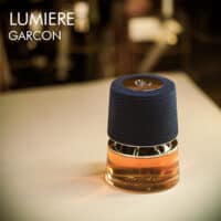 A 100ml bottle of French Avenue Lumiere Garcon Eau de Parfum with a orange-ish liquid and blue cap on a white table
